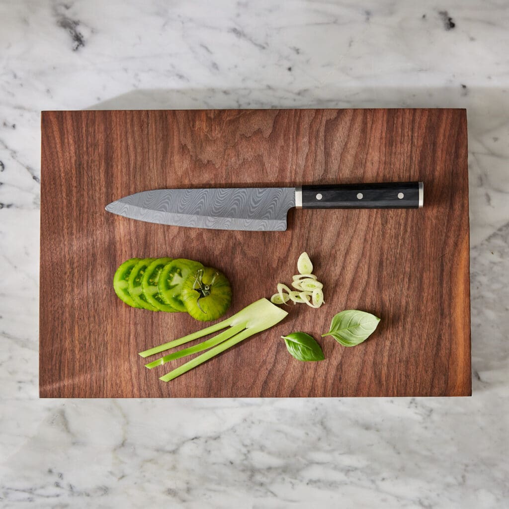 Damastmesser auf Holzbrett mit geschnittenen grünen Tomaten und Lauchzwiebeln.