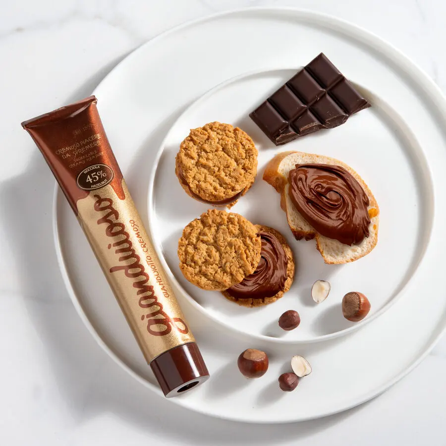 Gianduia Nuss-Nougat-Creme im edlen Tubenformat, serviert auf Brot und Keksen mit Haselnüssen und Schokolade