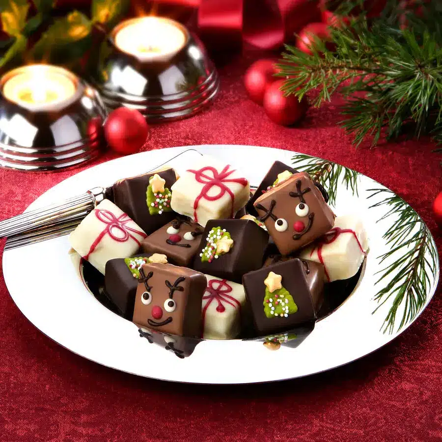 Festliche Petit Fours aus belgischer Schokolade, weihnachtlich dekoriert mit Rentier, Geschenk und Tannenbaum.