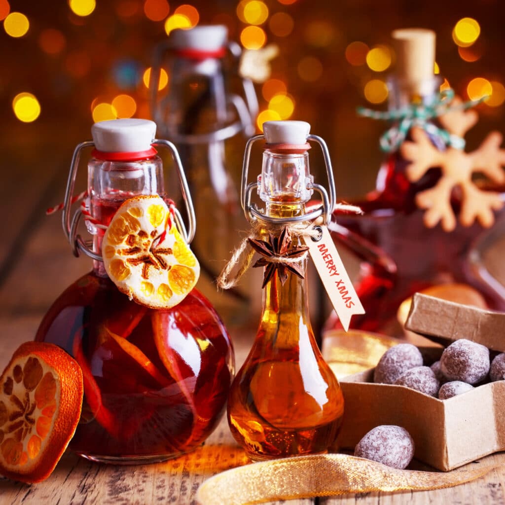 Hausgemachter Weihnachtslikör in Glasflaschen mit Orangen und Gewürzen, stimmungsvoll beleuchtet