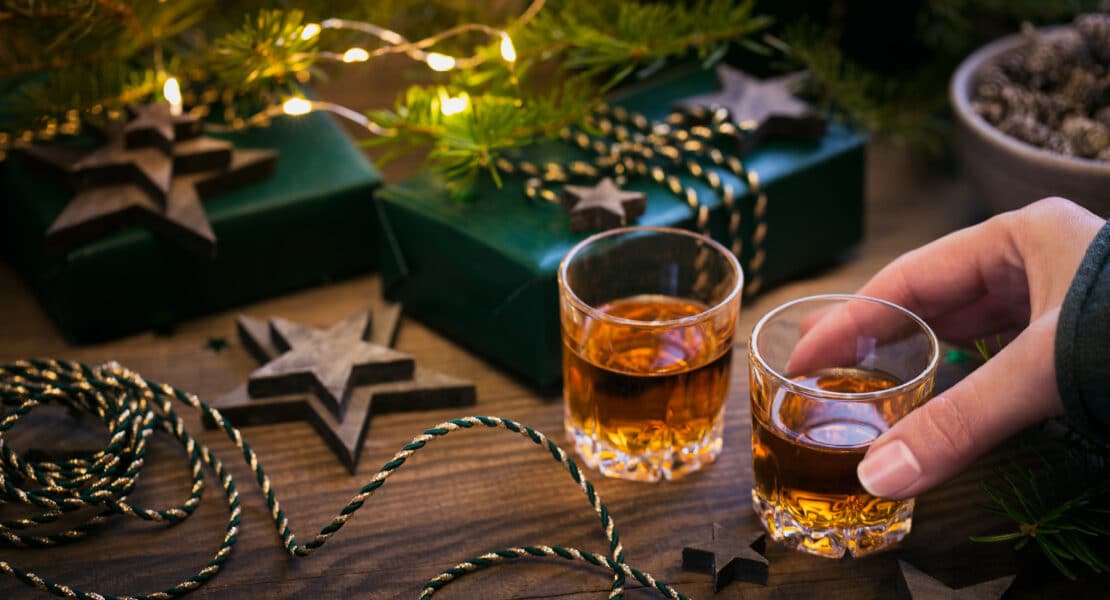 Zwei Gläser Weihnachtslikör auf Holztisch mit Tannenzweig, Stern-Deko und Geschenkverpackung