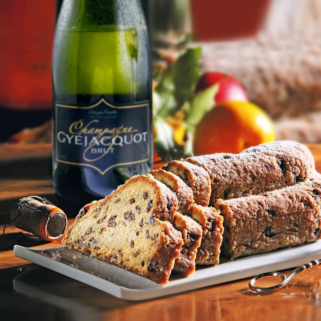 Saftiger Christstollen mit Rosinen und Mandeln, angerichtet neben einer Flasche Champagner auf festlicher Tafel