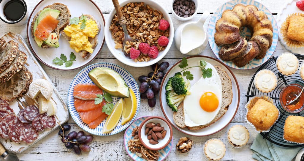 Frühstücks-Spread mit Avocado-Lachs-Brot, Rührei, Spiegelei auf Brot, Müsli mit Himbeeren, Kuchen und Gebäck