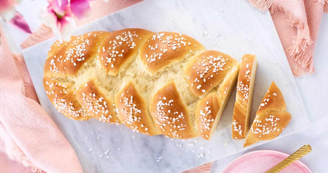 Hefezopf mit Hagelzucker auf Marmorplatte, teilweise angeschnitten, rosa Stoff im Hintergrund