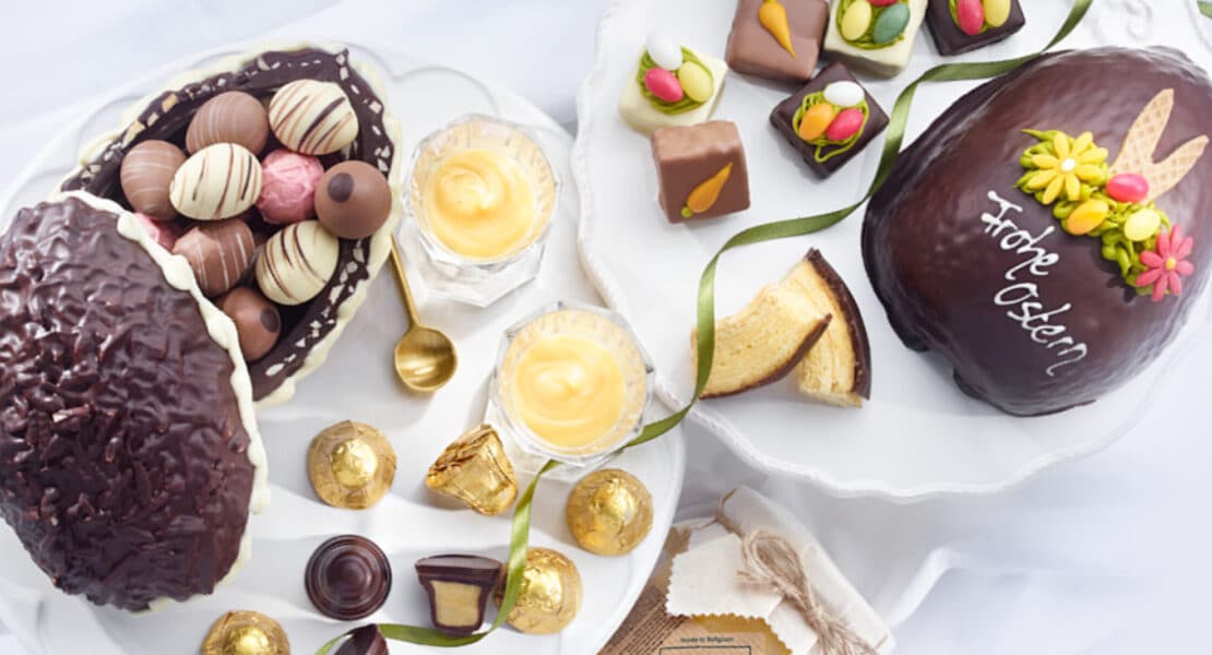 Verschiedene Osterpralinen, Ostergebäck und gefüllte Ostereier auf weißen Tellern arrangiert