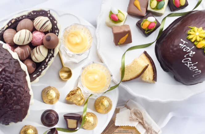 Verschiedene Osterpralinen, Ostergebäck und gefüllte Ostereier auf weißen Tellern arrangiert